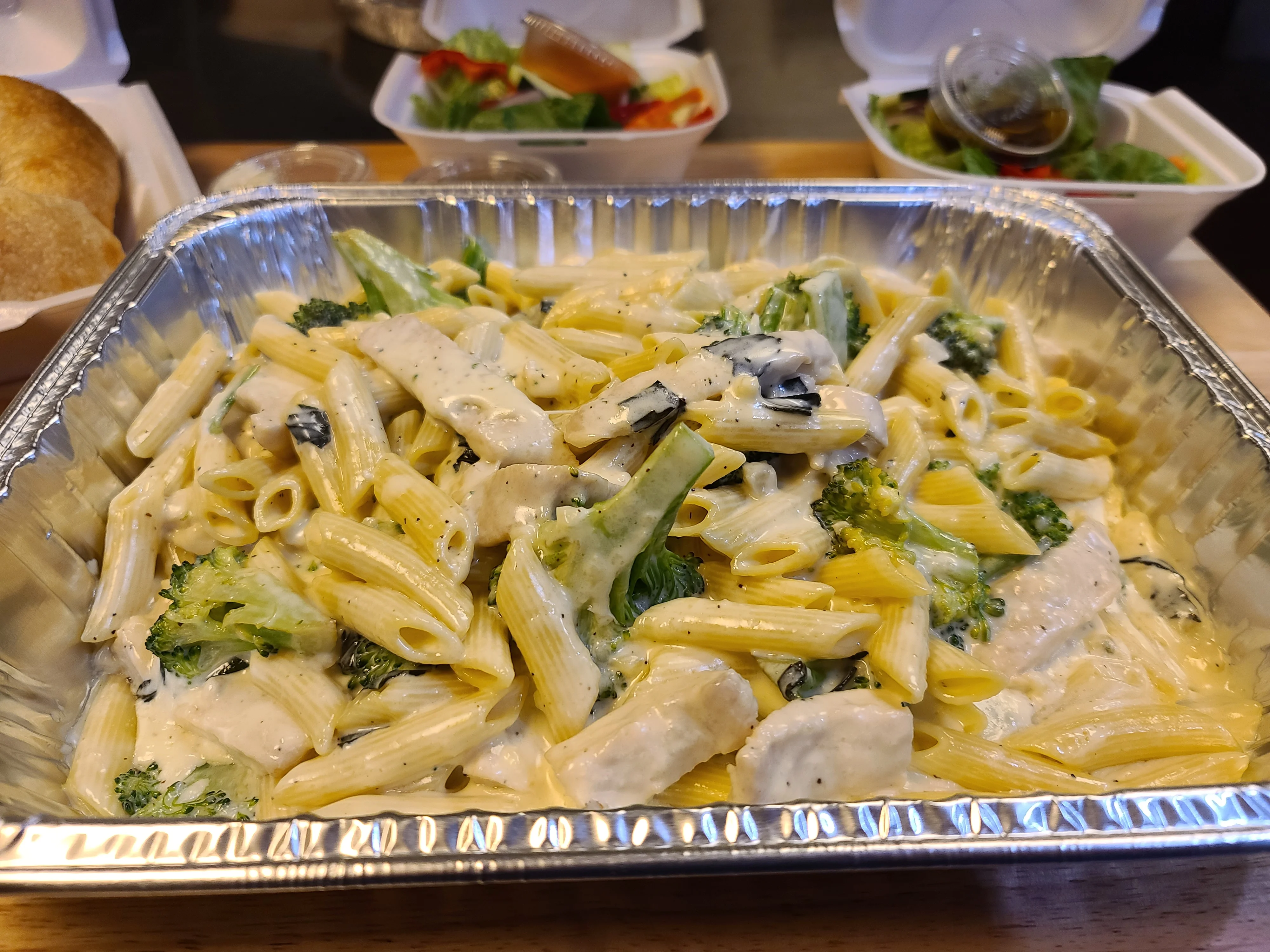 Family-style chicken pasta catering tray with salad and rolls