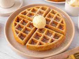 A golden waffle served on a plate, topped with a pat of butter and a sprinkle of sugar.