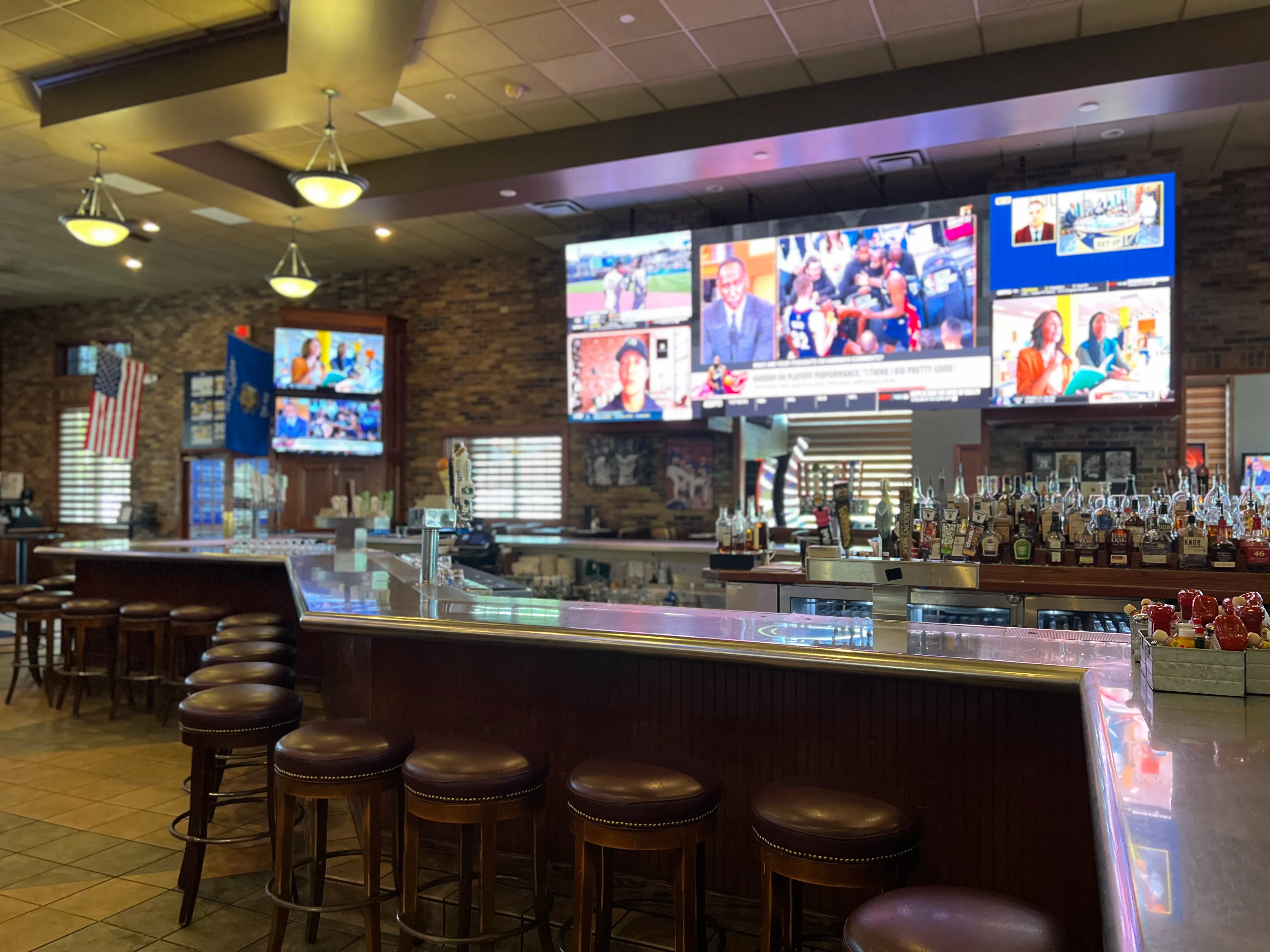 Interior of a bar with stools and multiple screens displaying sports.