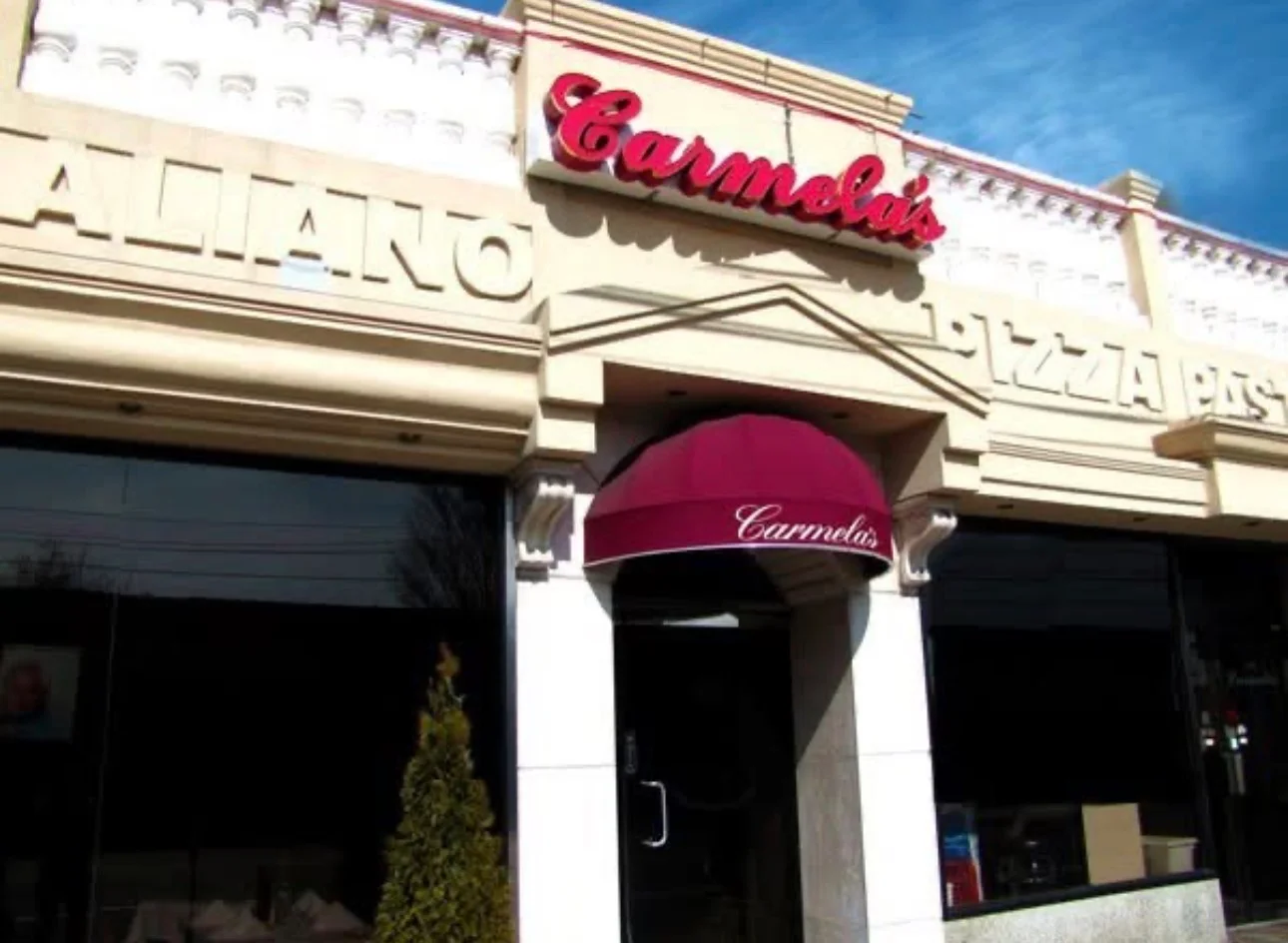 The exterior of a pizza restaurant named Carmela's, featuring a maroon awning and notable architectural details.