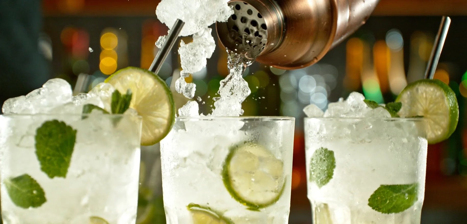 Cocktails featuring fresh mint and lime, with ice cascading into the glasses from a shaker.