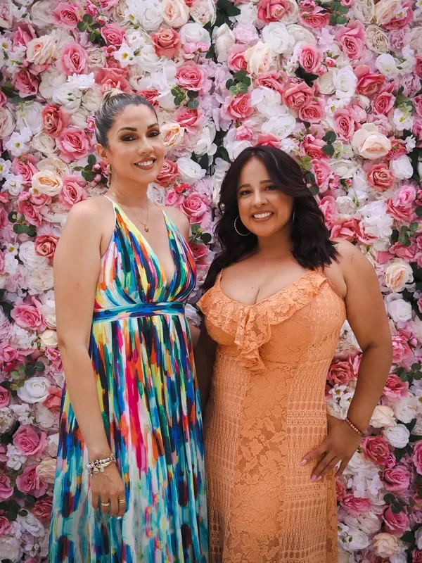 Two women posing in front of a floral backdrop