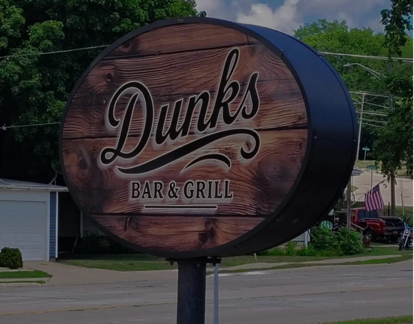 Guests dining inside Dunks Bar & Grill with food and drinks on the table, next to a large wooden wall sign reading “Dunks.”