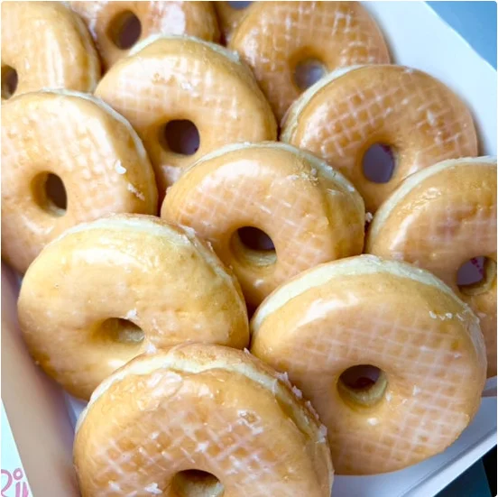 A box filled with glazed donuts, showcasing a shiny and smooth exterior.