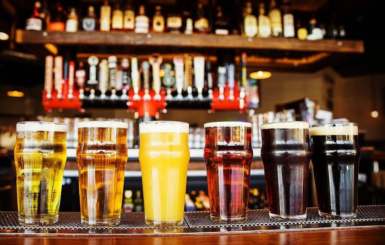 A variety of beers served in pint glasses displayed on a bar counter.