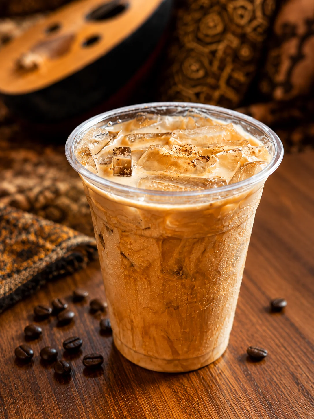 Iced coffee in a clear cup with ice cubes and coffee beans on a wooden table.
