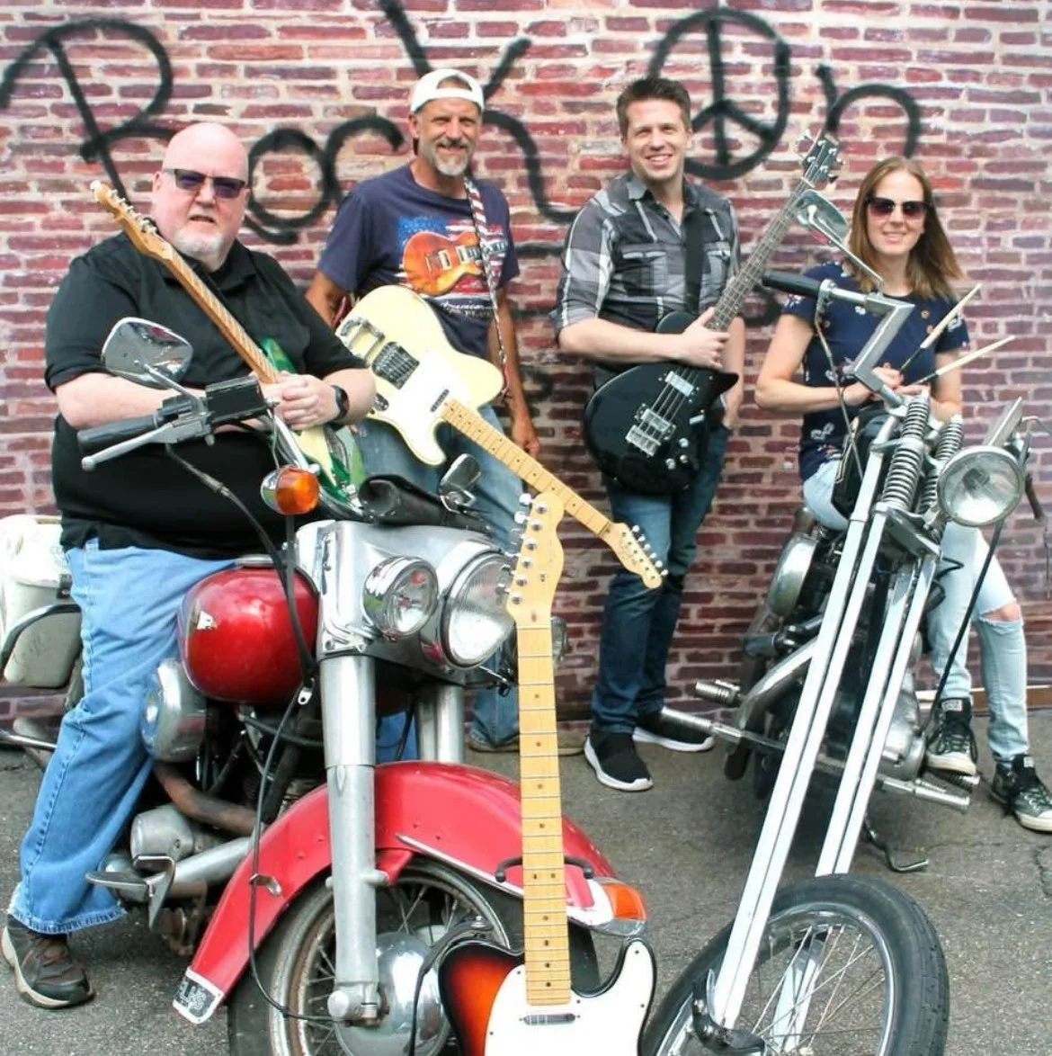 Band posing with guitars and motorcycles against a brick wall