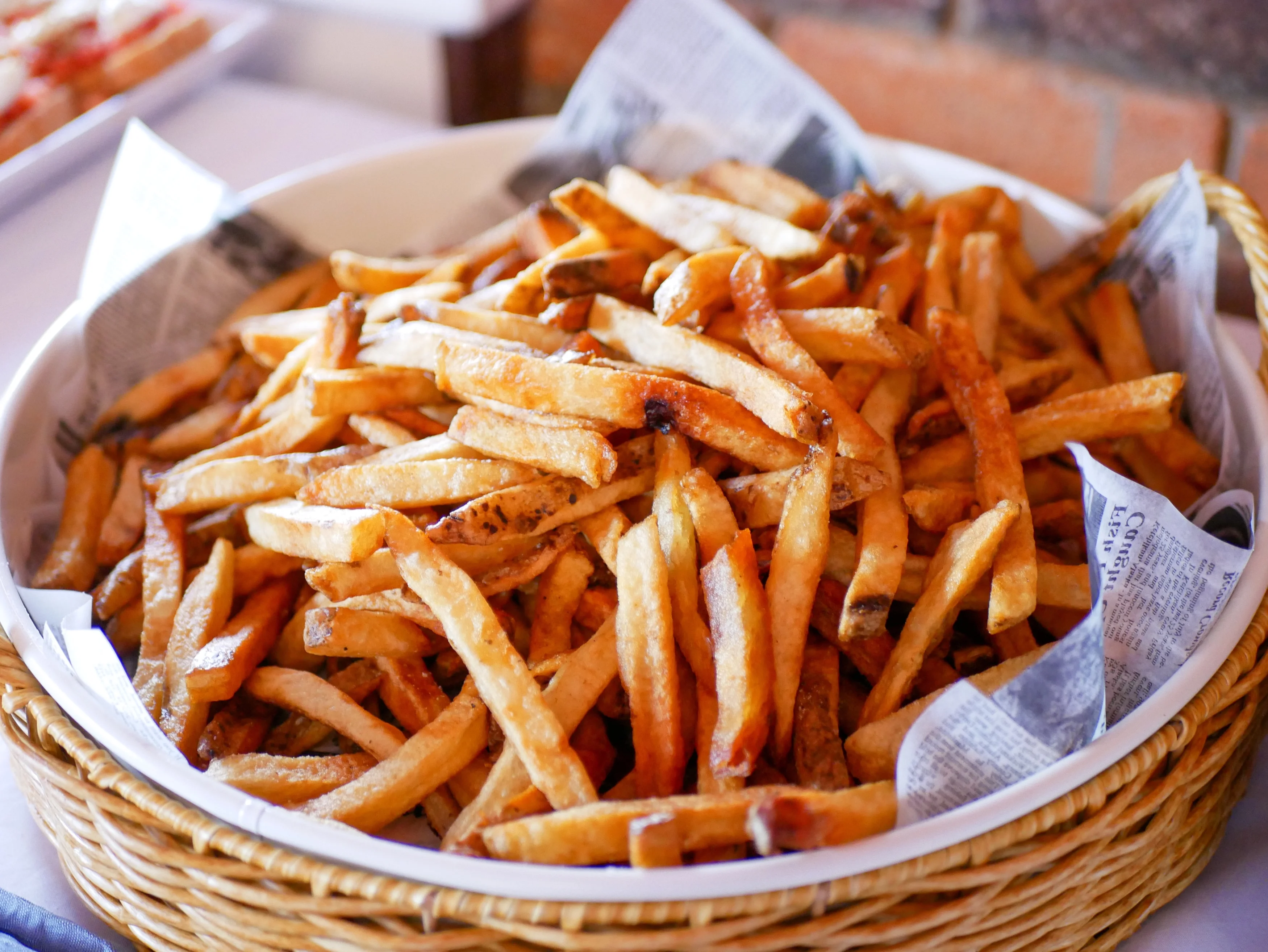A large basket filled with golden, crispy French fries, served with newspaper for presentation.