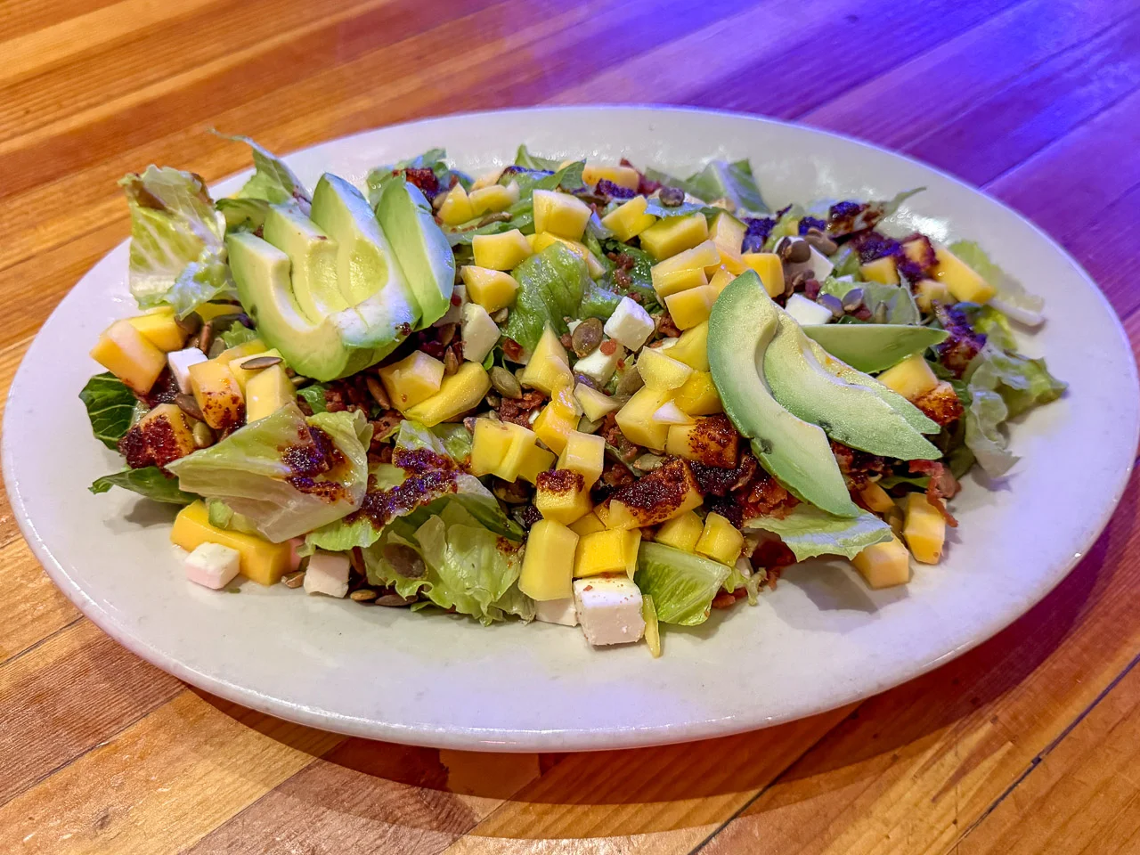 Mango & Avocado Salad is made with romaine hearts, queso fresco, bacon, toasted pumpkin seeds, chile de árbol oil + pumpkin seed-honey vinaigrette