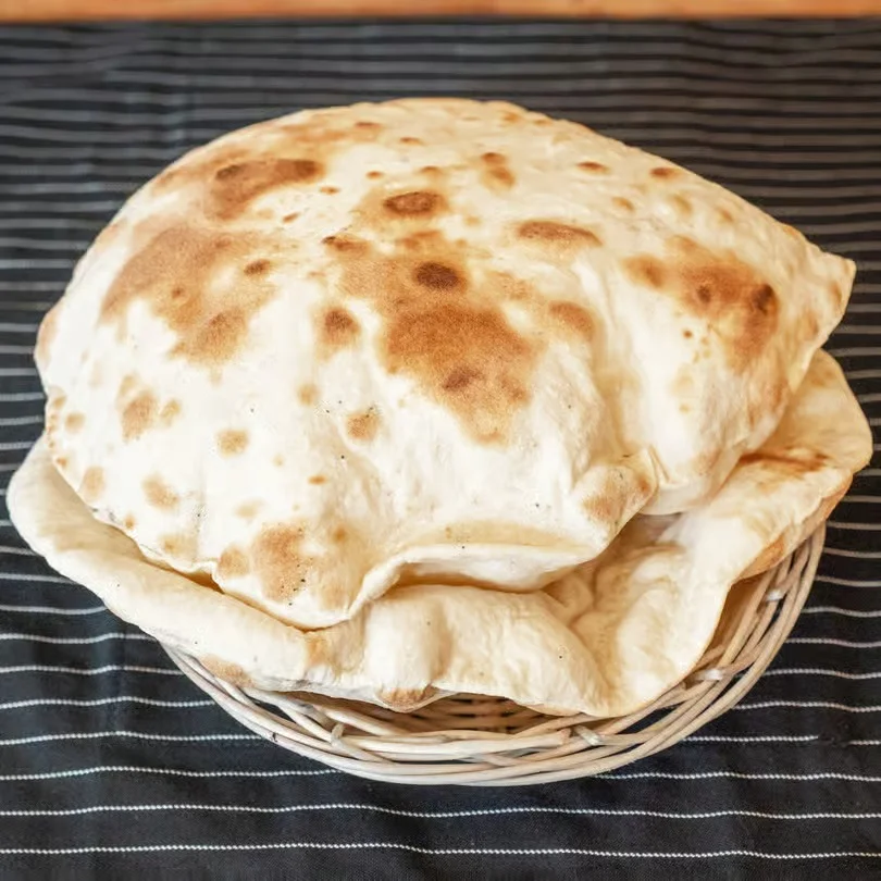 A basket of freshly baked, fluffy naan bread on a striped tablecloth.