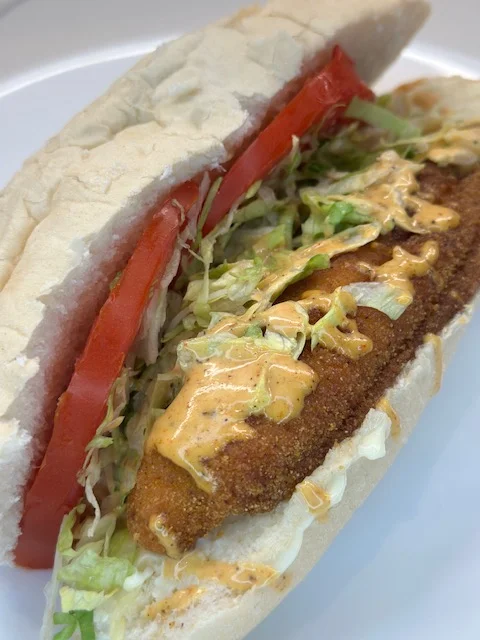 A sandwich filled with a crispy fried fillet, topped with lettuce, tomatoes, and a creamy sauce, all housed in a soft bun.