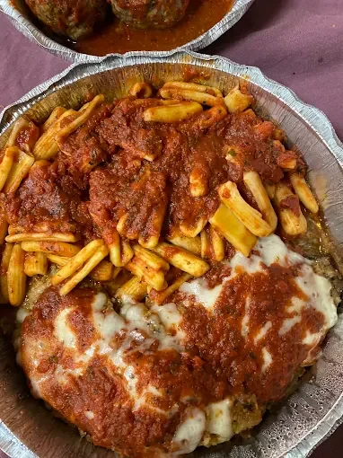 A serving of pasta topped with a hearty meat sauce and melted cheese. Served alongside meatballs in a saucy broth.