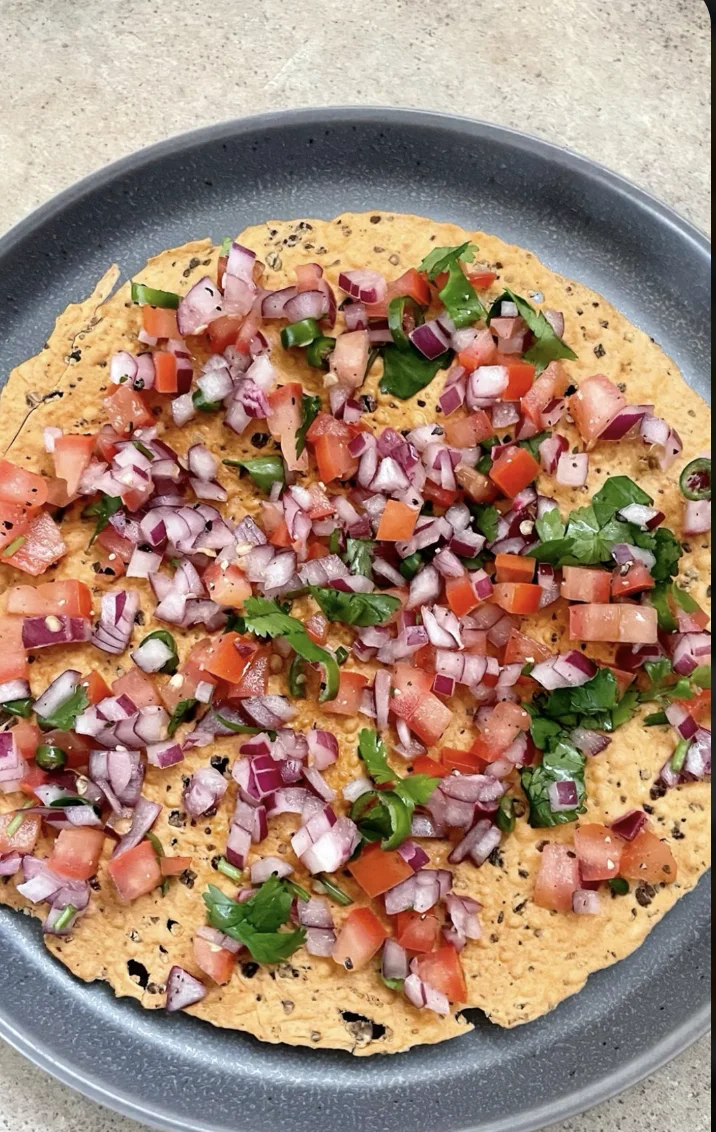 A flatbread topped with a colorful mix of diced tomatoes, onions, and fresh herbs, showcasing vibrant ingredients.