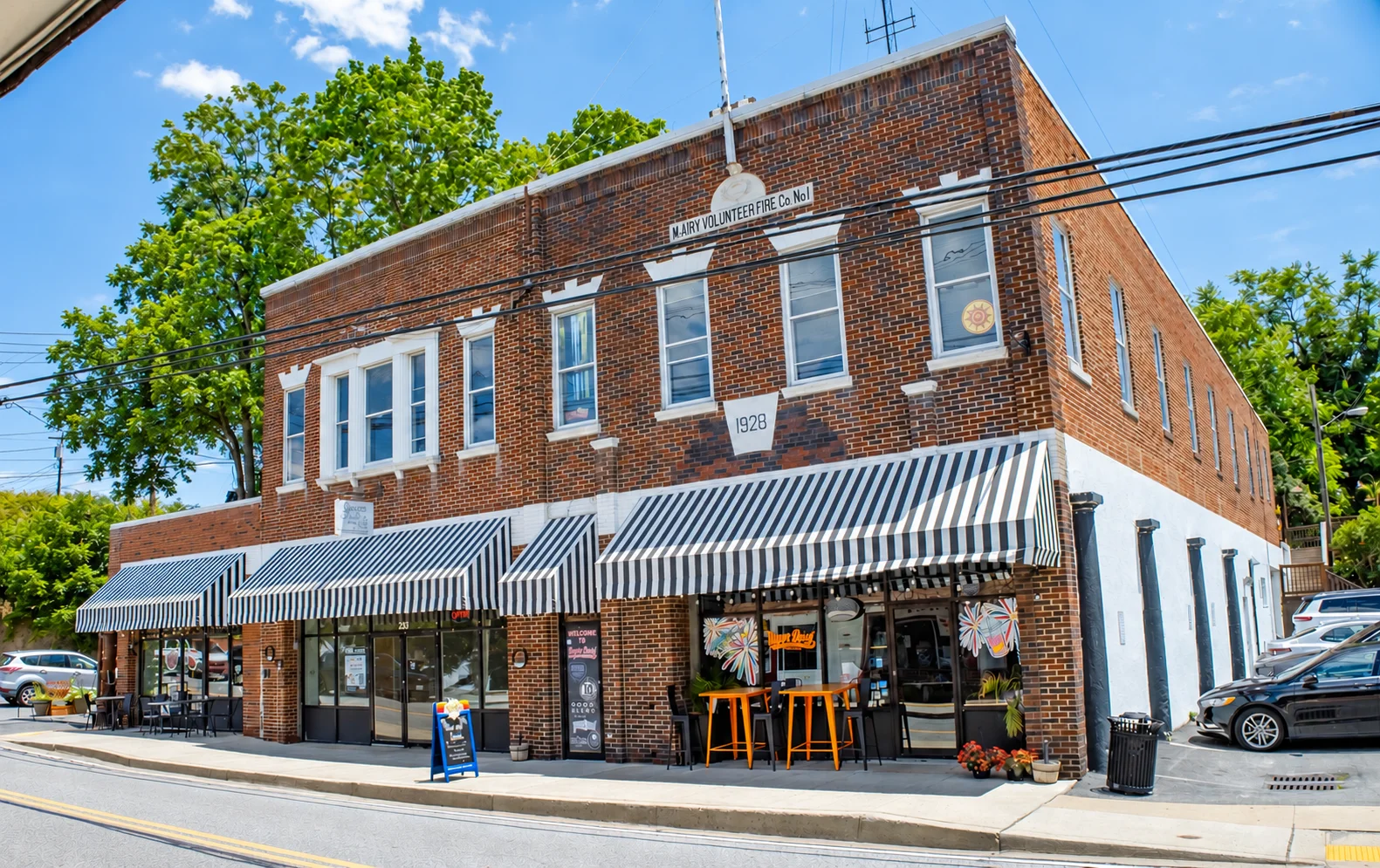 Tilted street view of a brick restaurant storefront with striped awnings and sidewalk signs