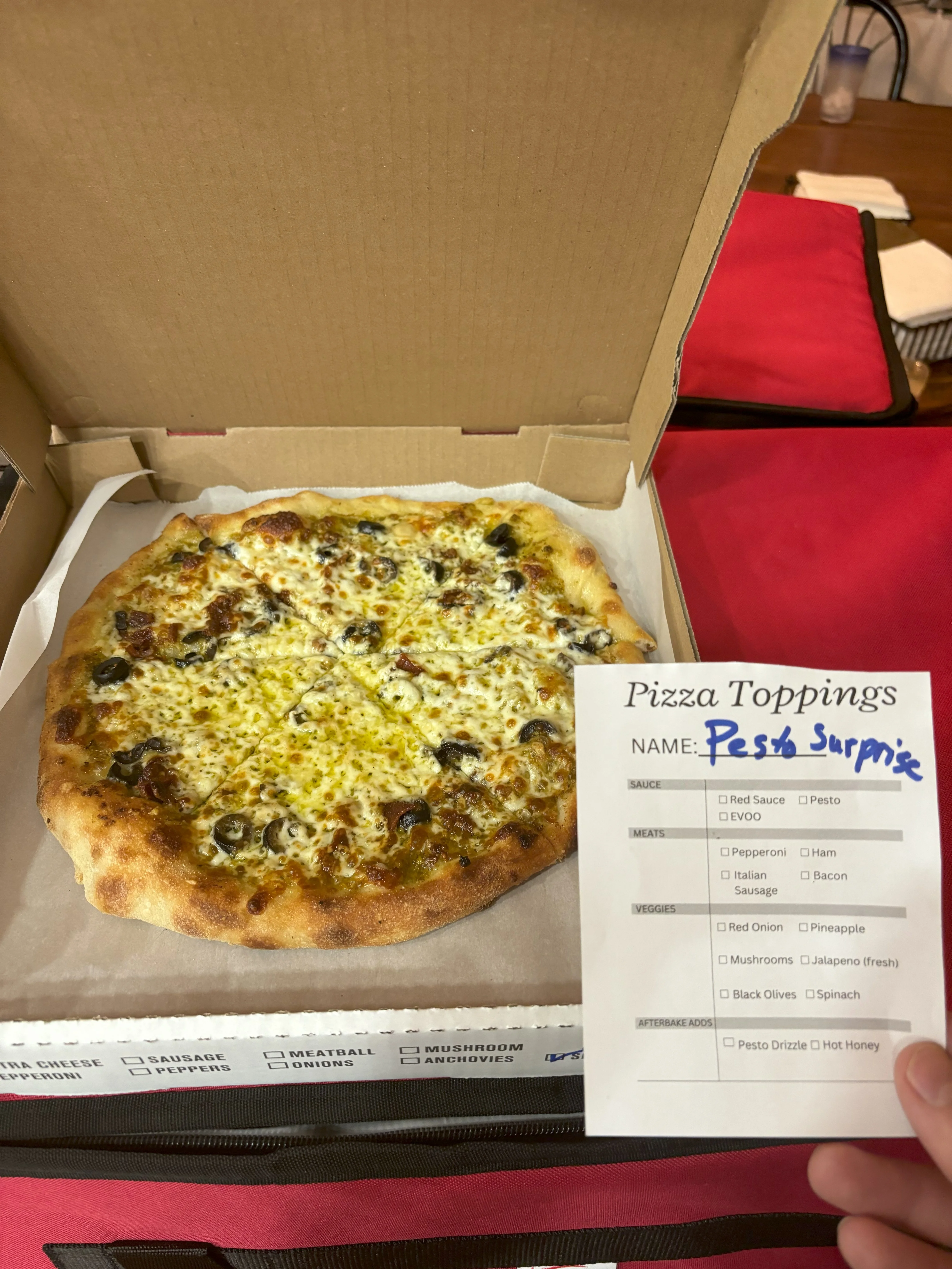 Pesto pizza with olives and cheese in a pizza box