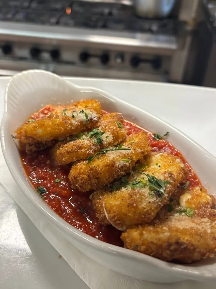 Crispy fried cheese bites served over a rich tomato sauce, garnished with herbs.