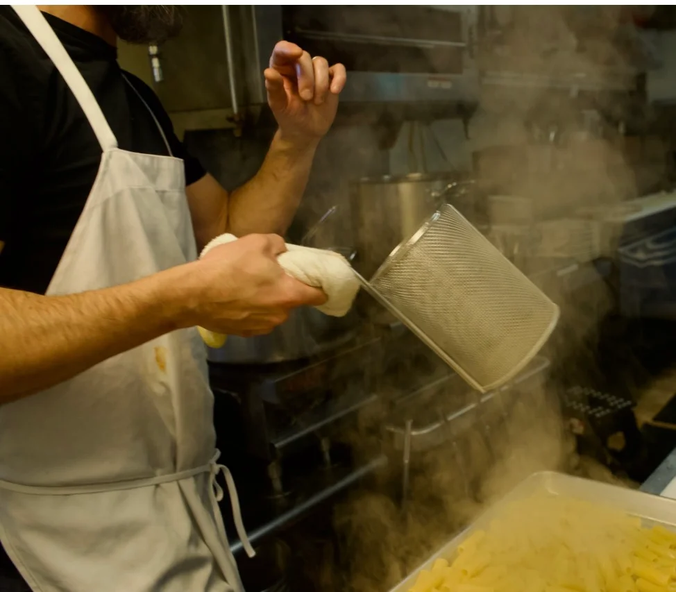 Chef straining pasta in a busy kitchen
