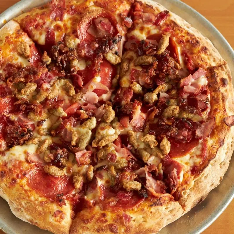 A large pizza topped with pepperoni, various meats, and a golden crispy crust, sitting on a metal tray.