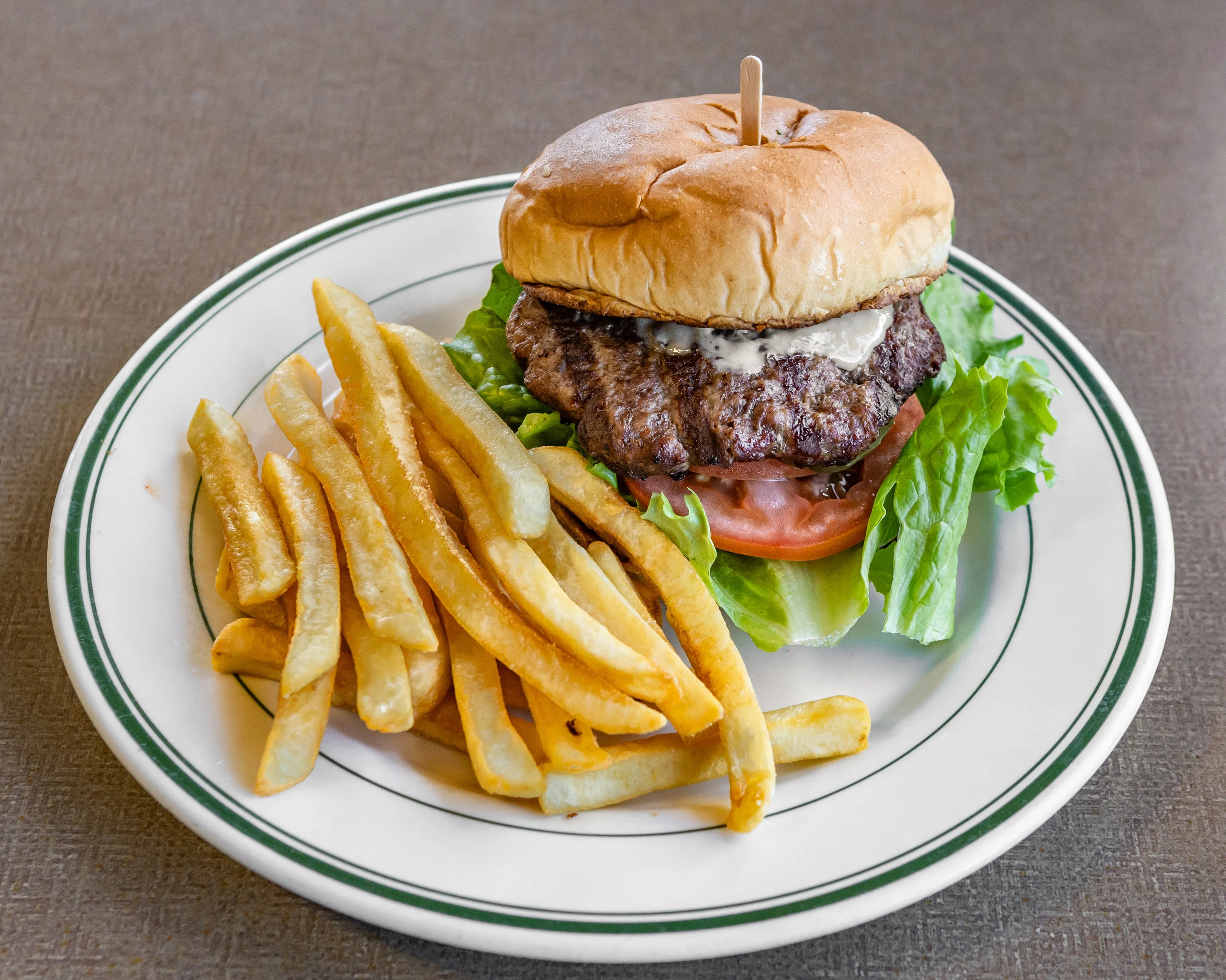A hamburger served with lettuce and tomato, accompanied by a side of golden French fries on a white plate.