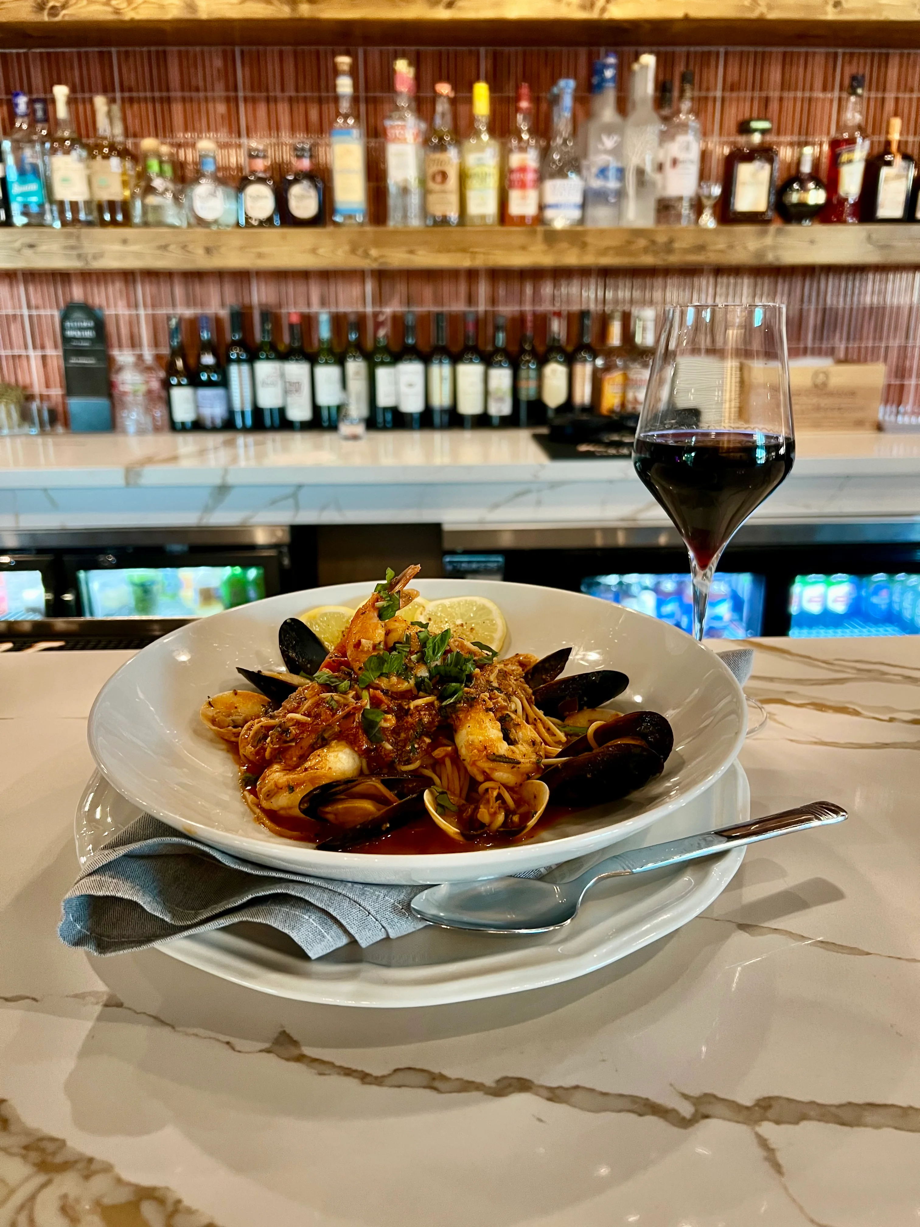 A flavorful seafood pasta dish featuring shrimp and mussels, served with a side of wine in a cozy bar setting.