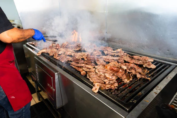 Grilling marinated meat on a barbecue grill with smoke rising.