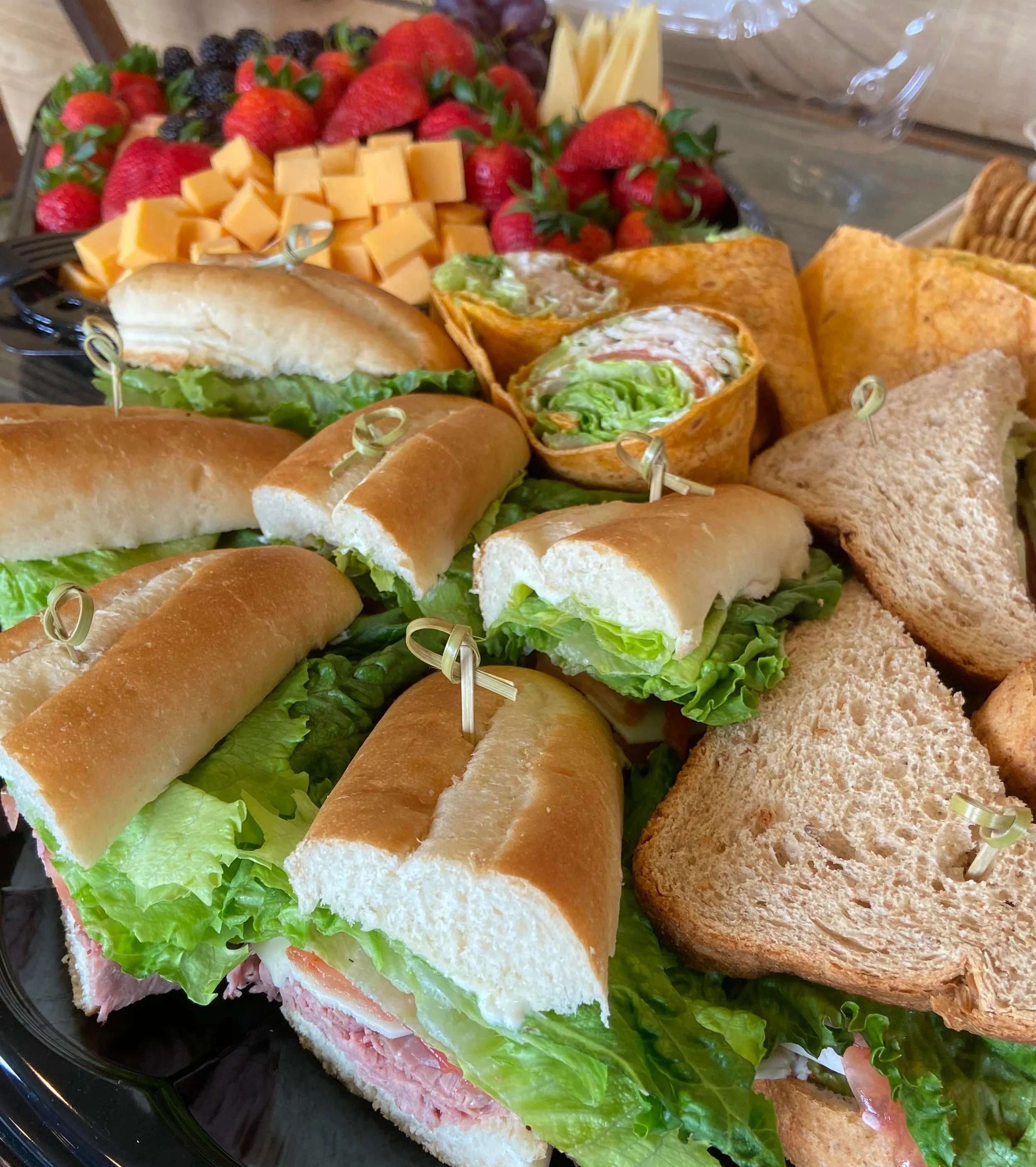 A lively gathering in a cozy shop, featuring a display of desserts, a group of people enjoying a celebration, and a beautifully arranged charcuterie spread.