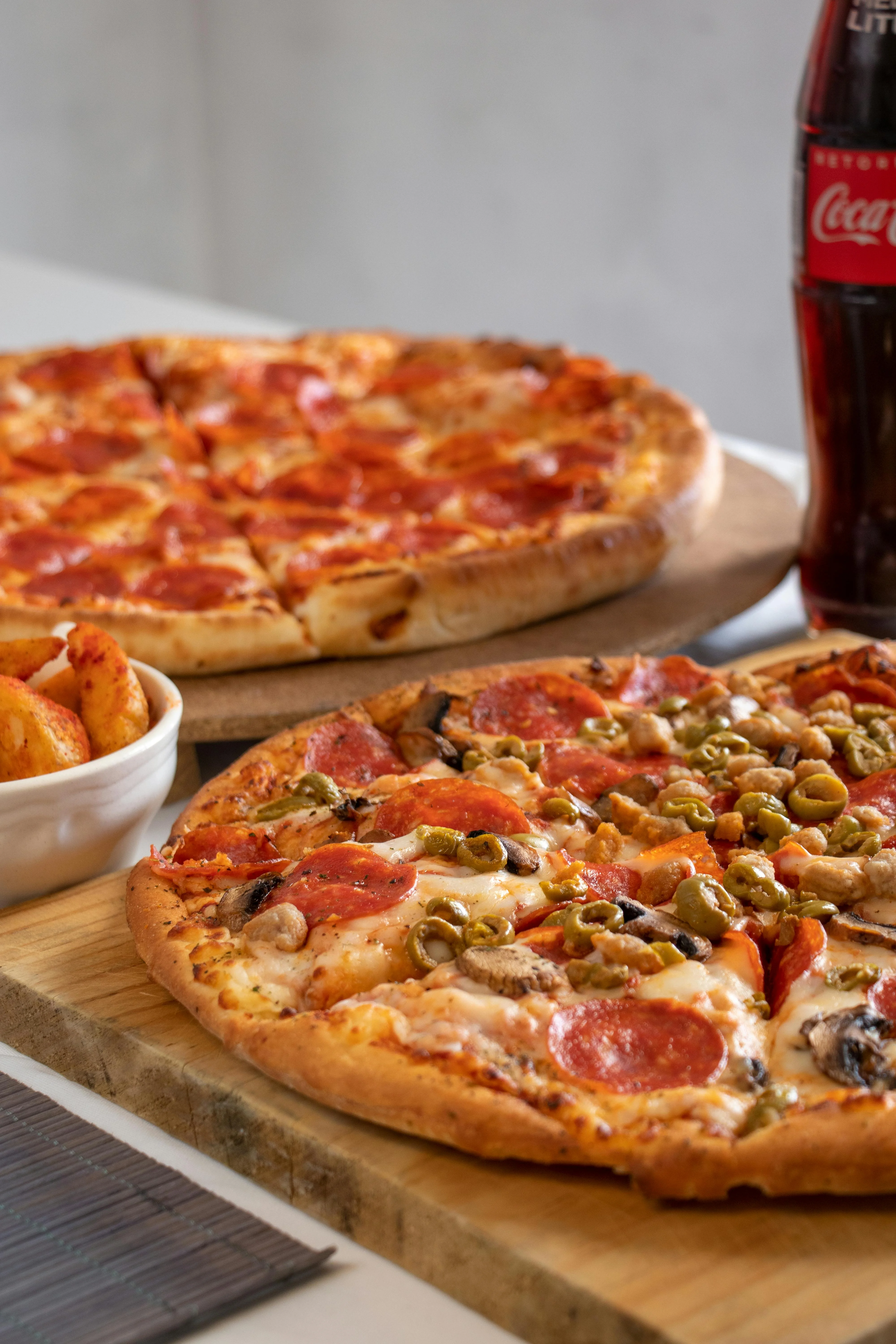 Close-up of pepperoni and veggie pizzas served at Nina's Pizzeria and Italian Restaurant in Chittenango, NY with a side of potato wedges