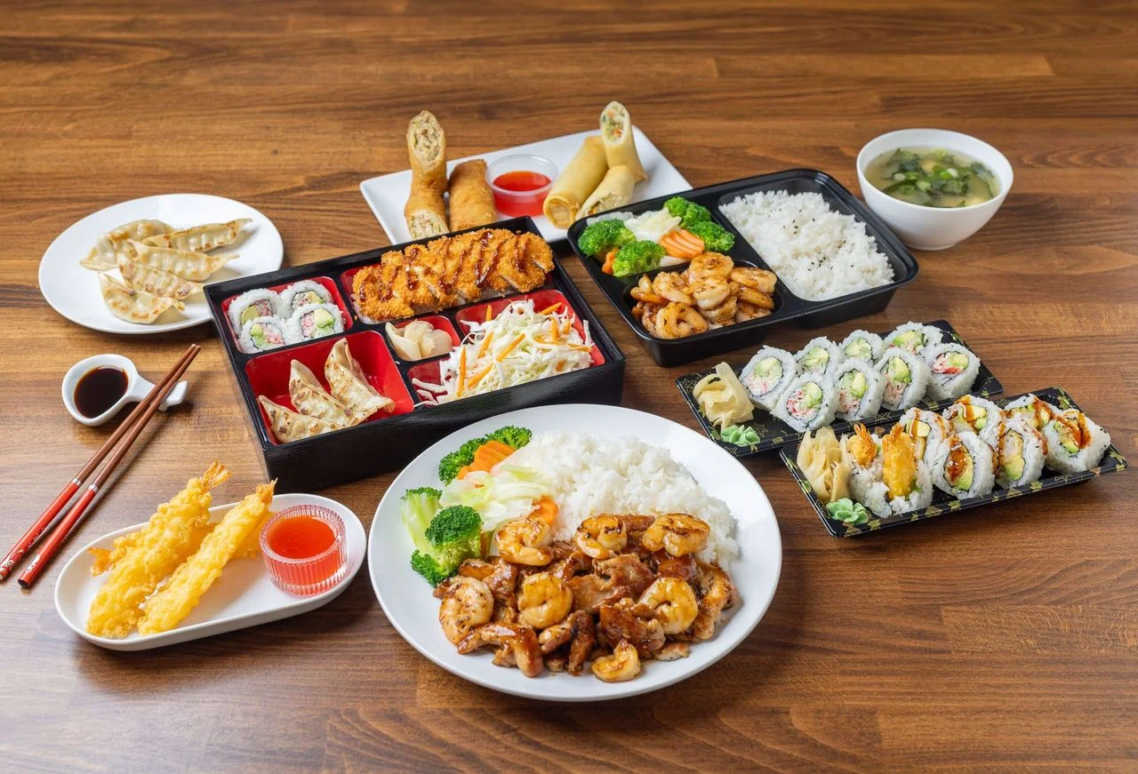 A delicious Asian meal with chicken, sushi, spring rolls, and a drink.