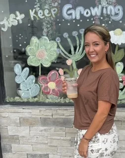 Smiling woman holding a drink in front of a colorful mural
