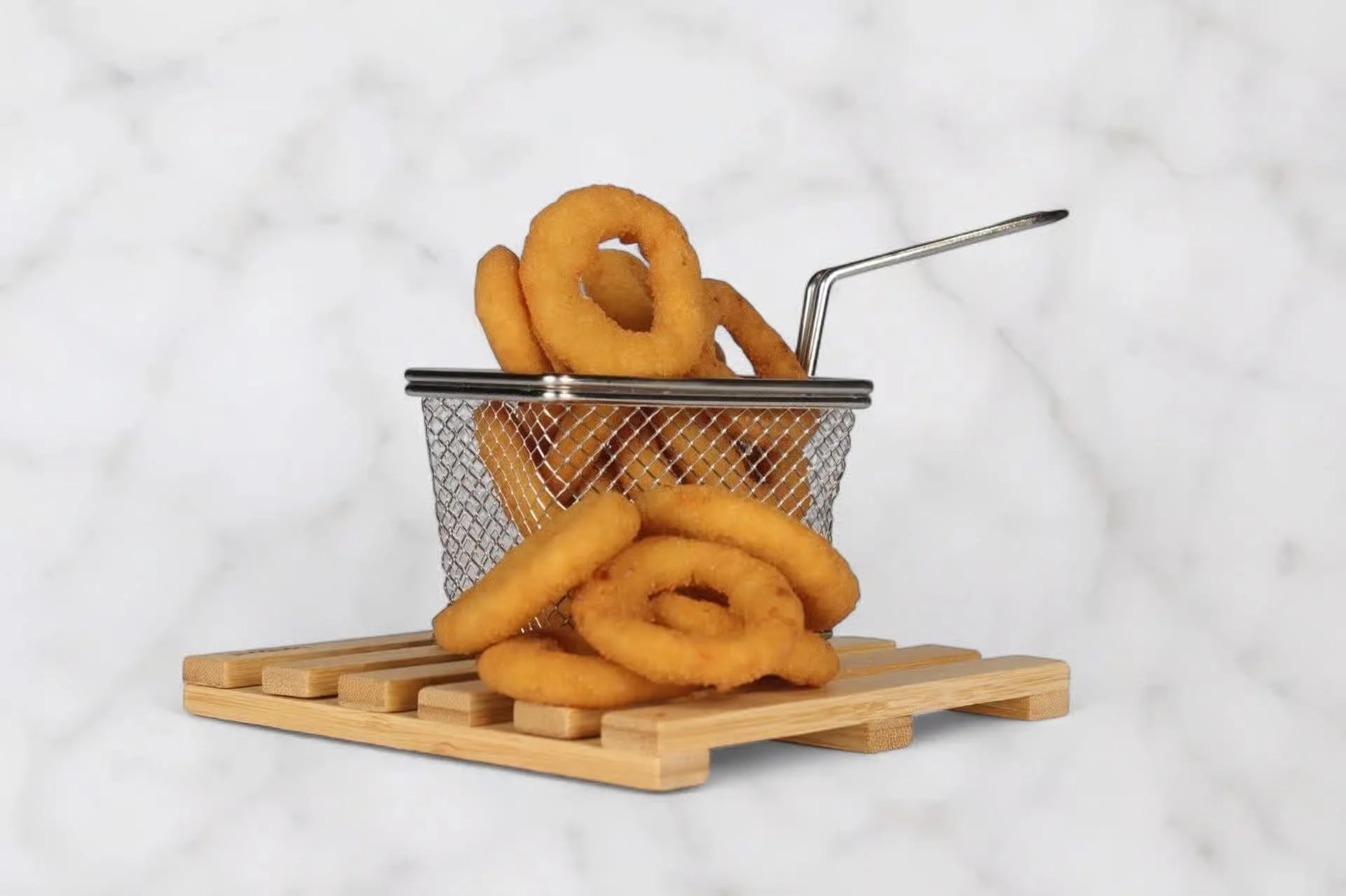 A small metal basket filled with golden-brown onion rings, served on a wooden board.