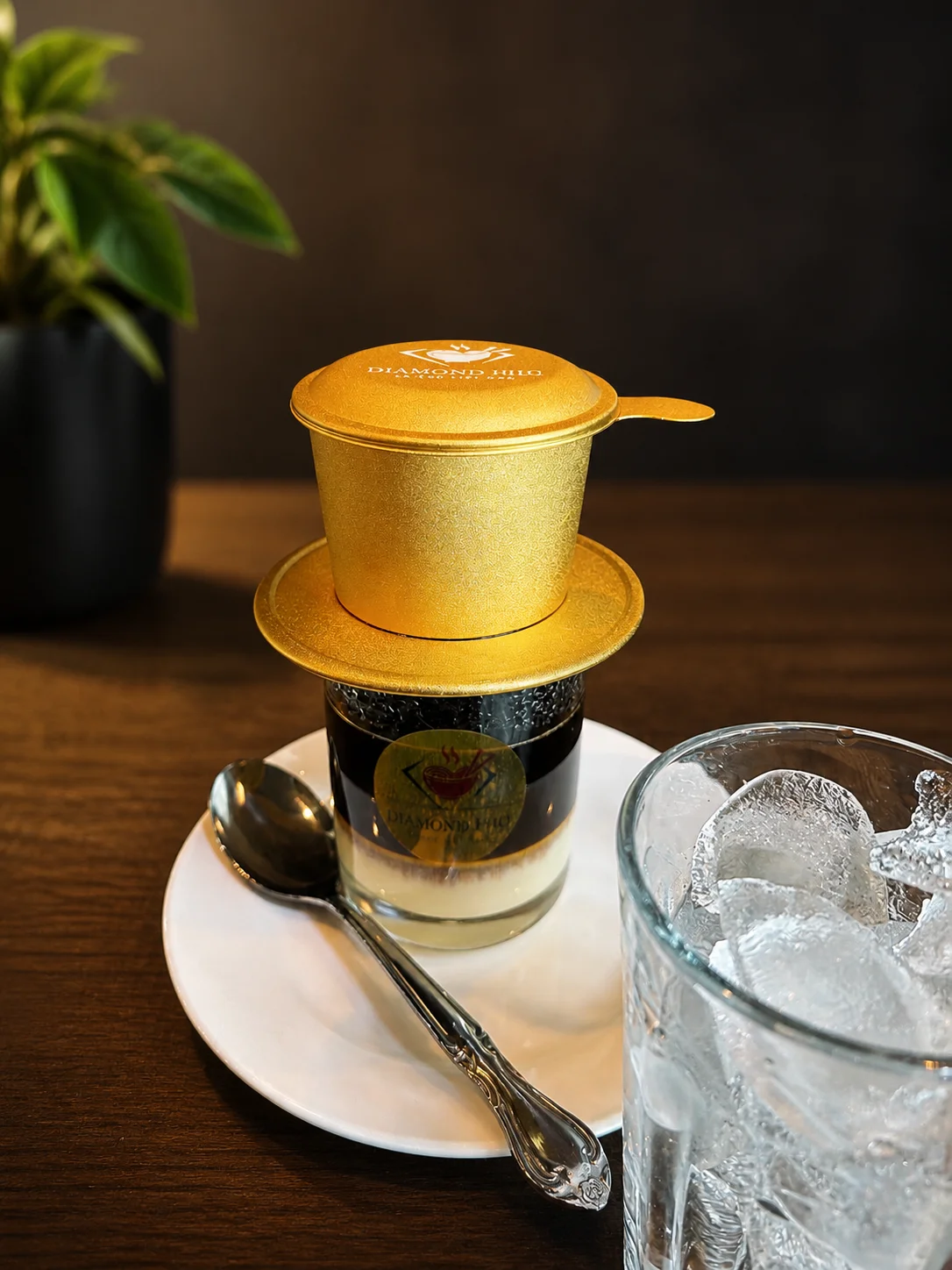 A golden coffee capsule atop a layered dessert with a spoon and glass of ice.