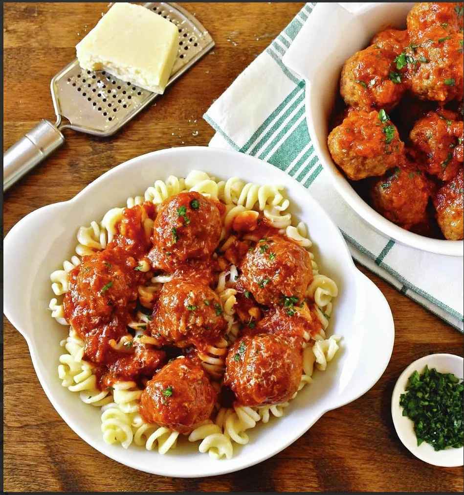 Pasta with meatballs in marinara sauce, garnished with parsley.