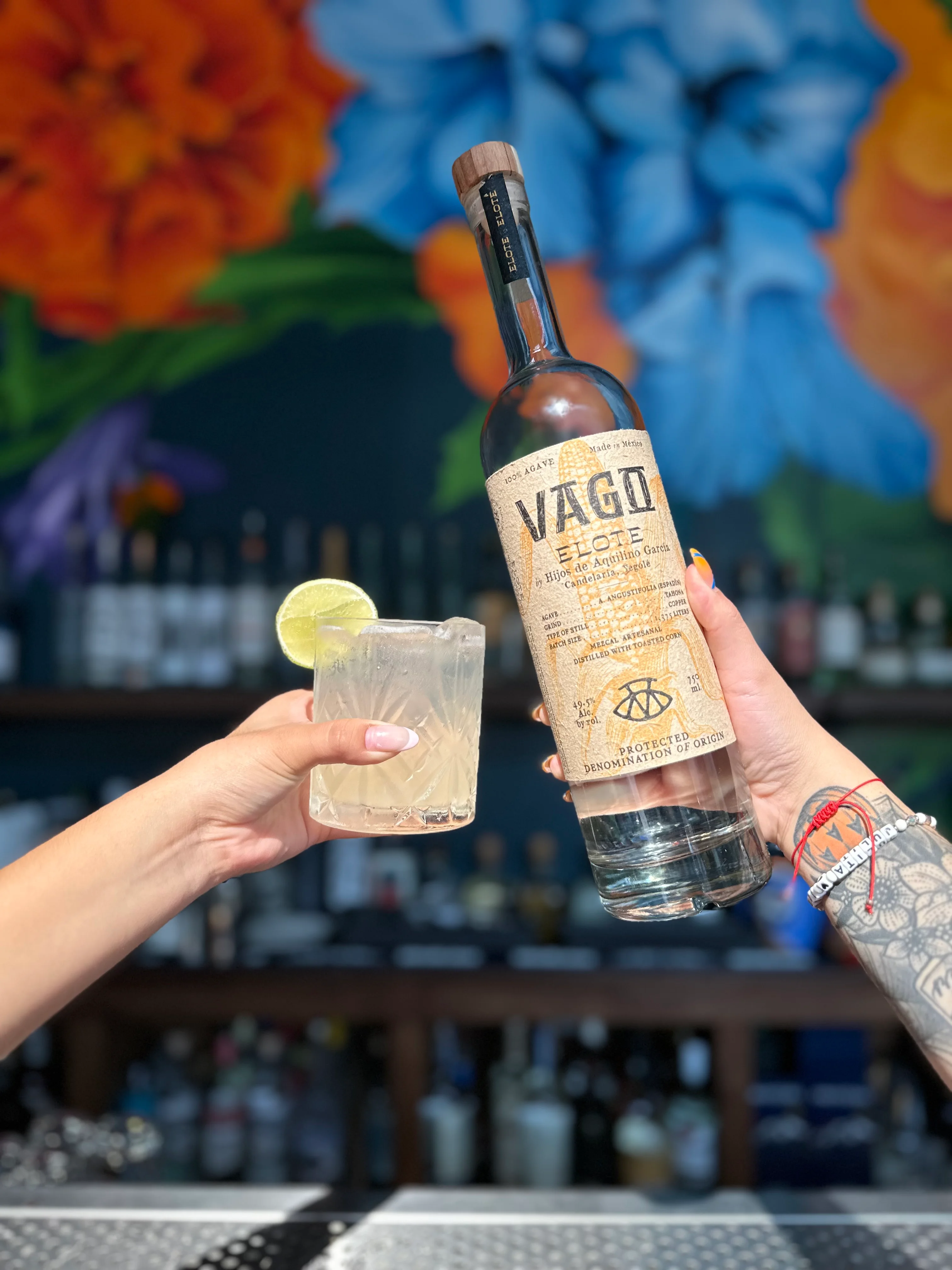 Bartender showcasing Vago mezcal and cocktail at a vibrant bar