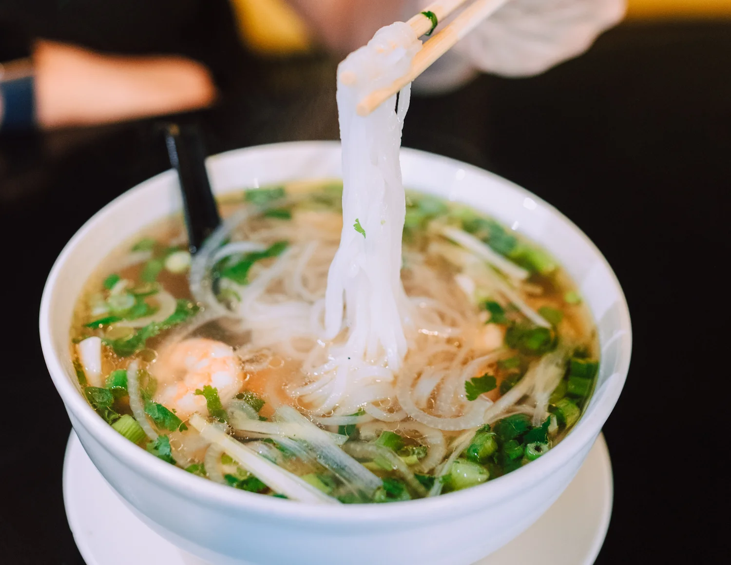 A hand wearing a glove is sprinkling an ingredient from a bowl in a kitchen setting.