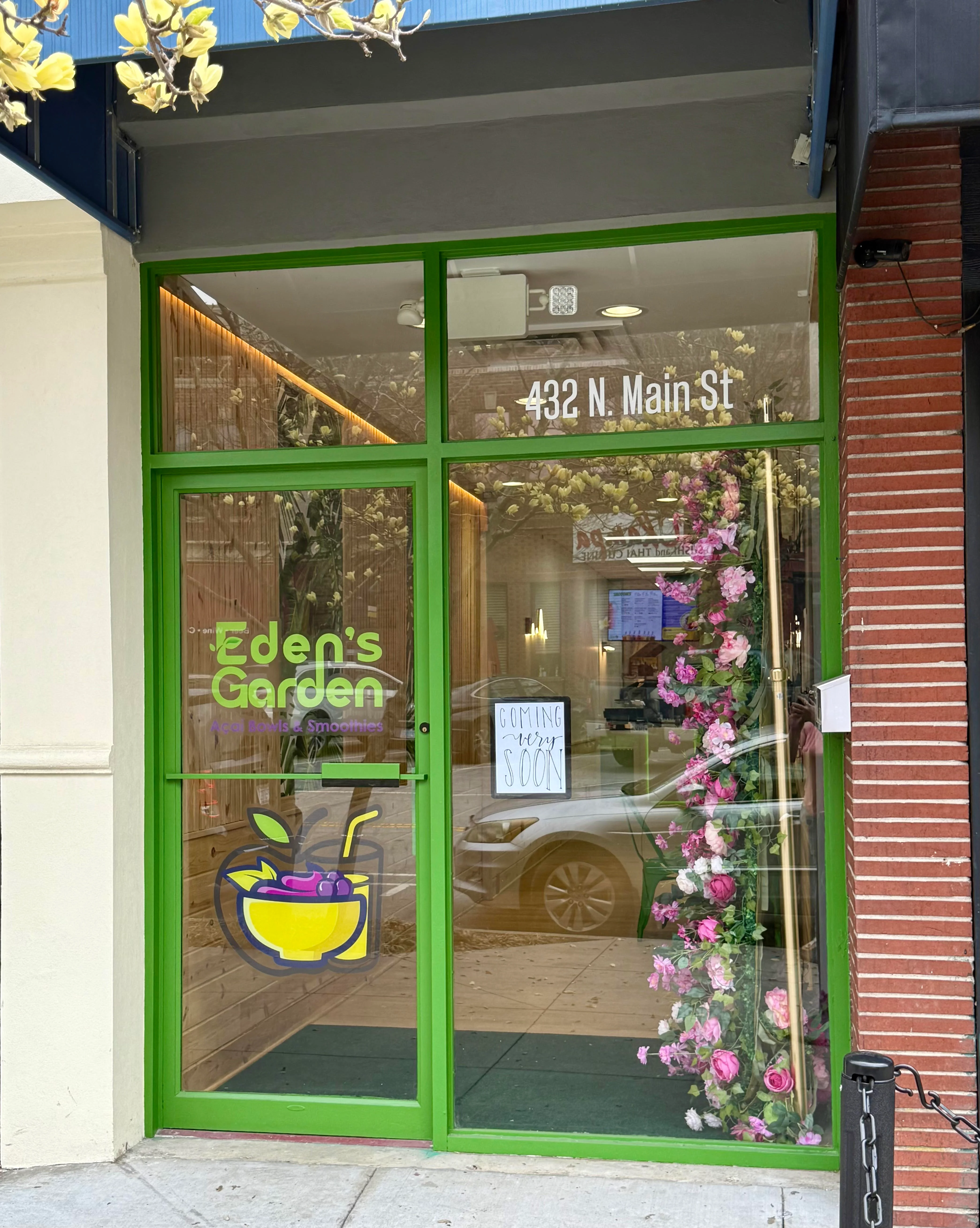 A storefront displaying colorful signage and floral decorations, indicating a smoothie and ice bowl shop called 'Eden's Garden'.