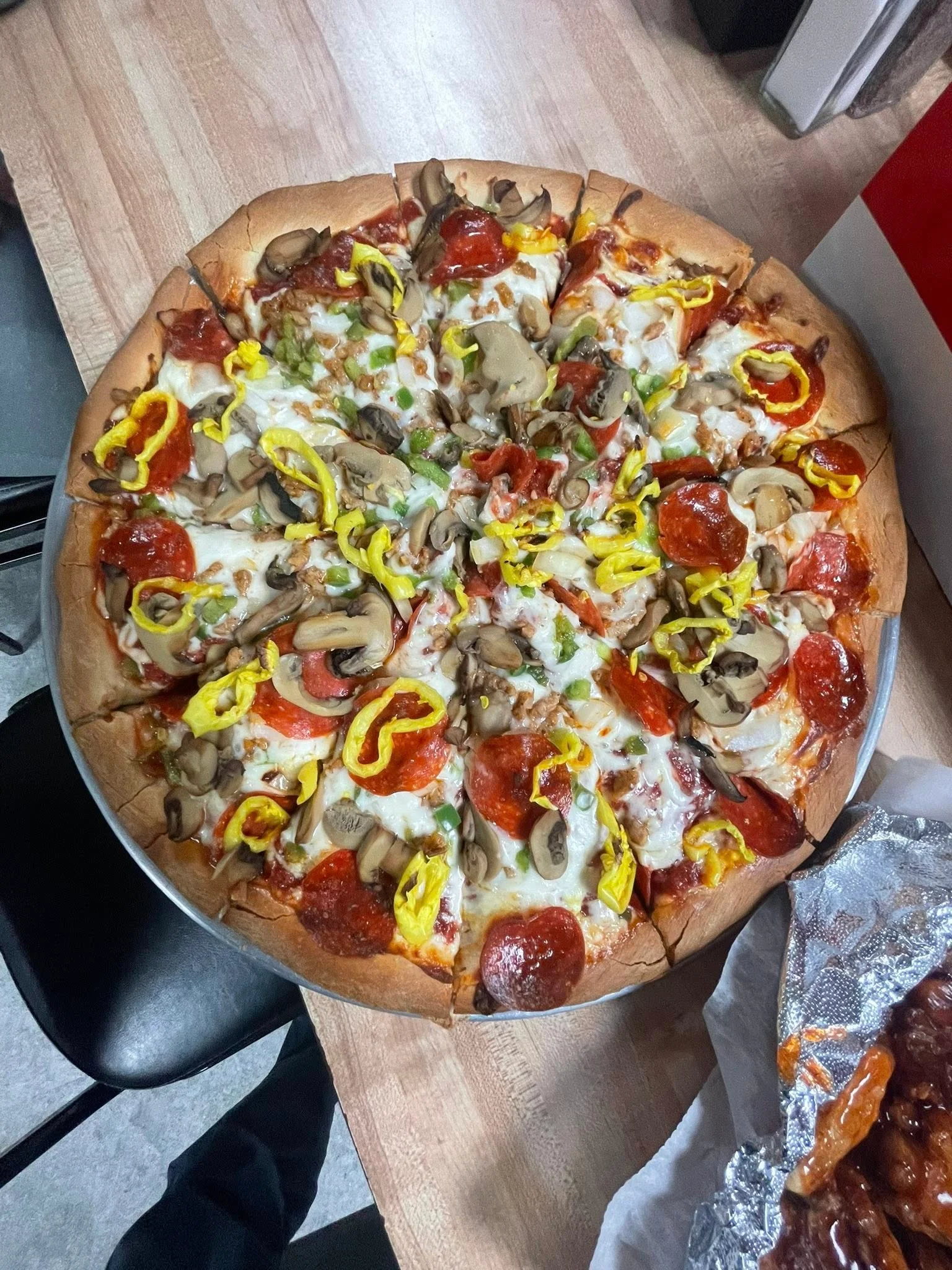 A large pizza sliced into pieces, topped with pepperoni, mushrooms, green peppers, and yellow peppers.