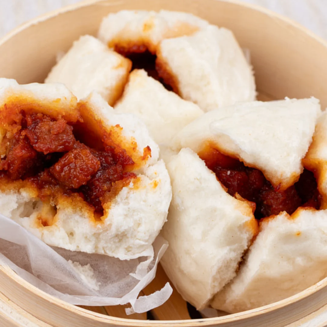 Steamed buns filled with savory meat, served in a bamboo steamer.