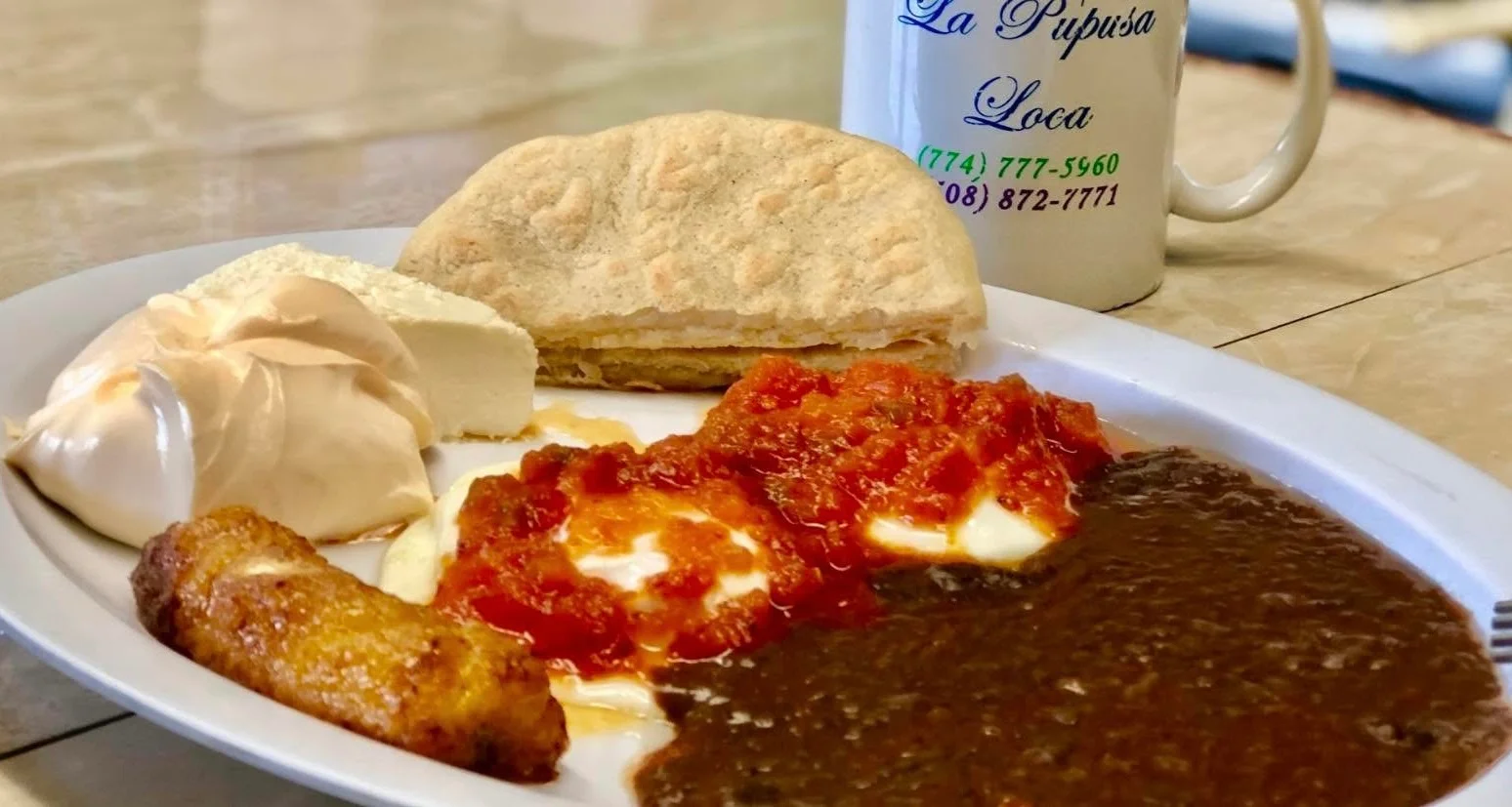 A delicious plate featuring a variety of dishes, including soft beans, eggs topped with red sauce, a sweet dessert, a portion of cheese, and fried plantains, served alongside a traditional bread.