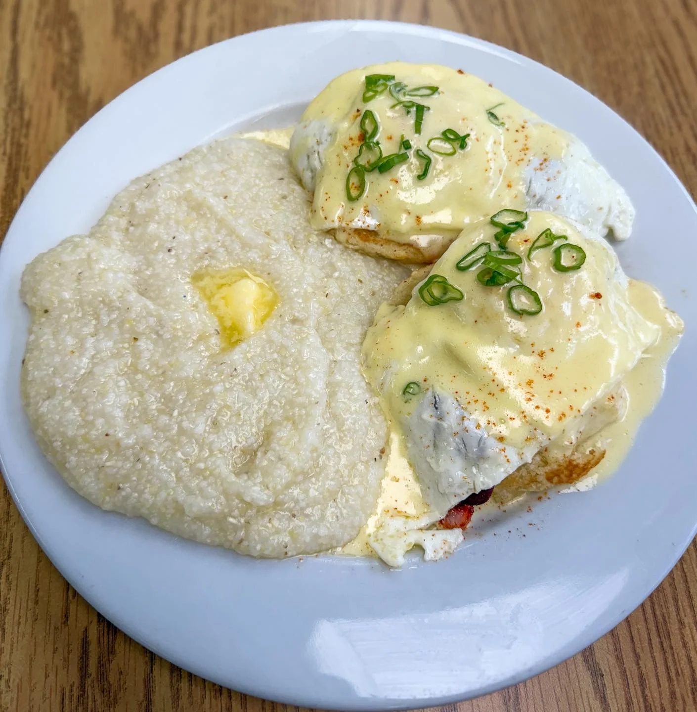 A delicious plate featuring poached eggs on biscuits topped with hollandaise sauce and green onions, served with a side of creamy grits.