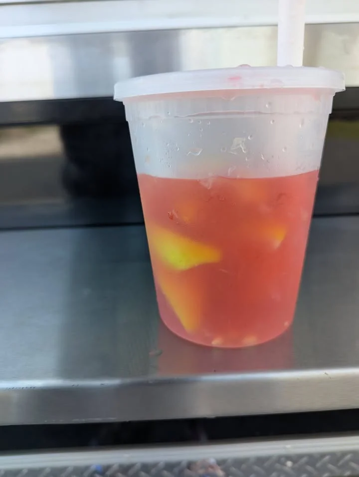 A chilled drink in a cup filled with a pink fruity beverage and pieces of fruit.