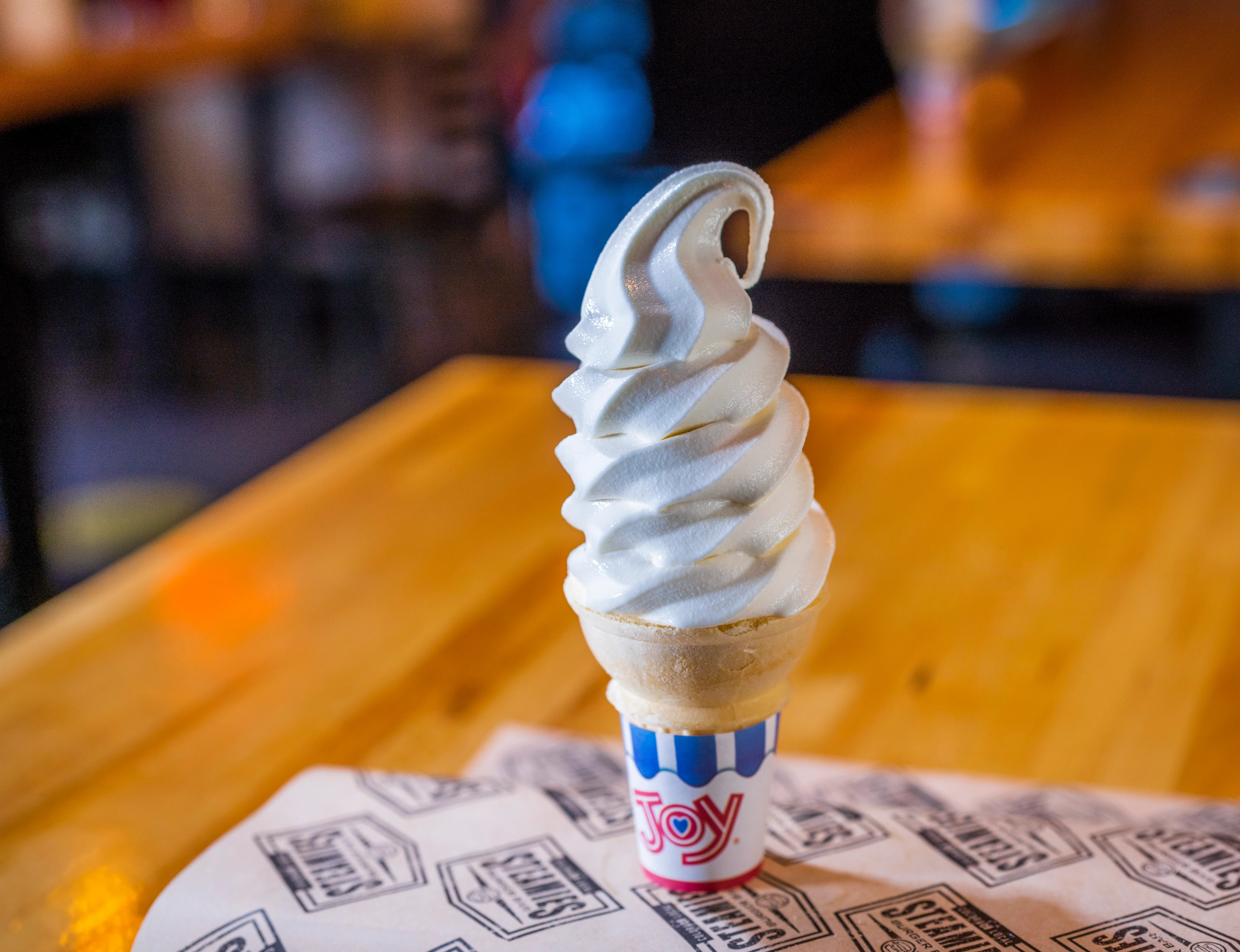 A soft serve ice cream cone with a perfectly swirled top, served in a striped paper cup.