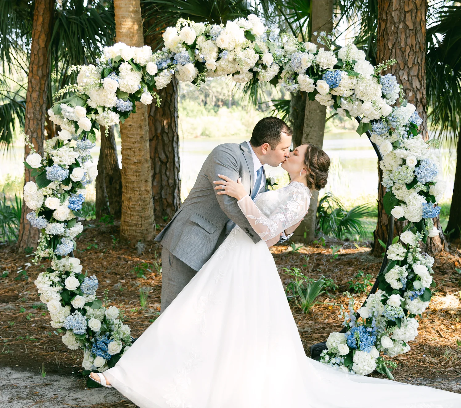 Bride and groom kissing under floral arch at outdoor wedding