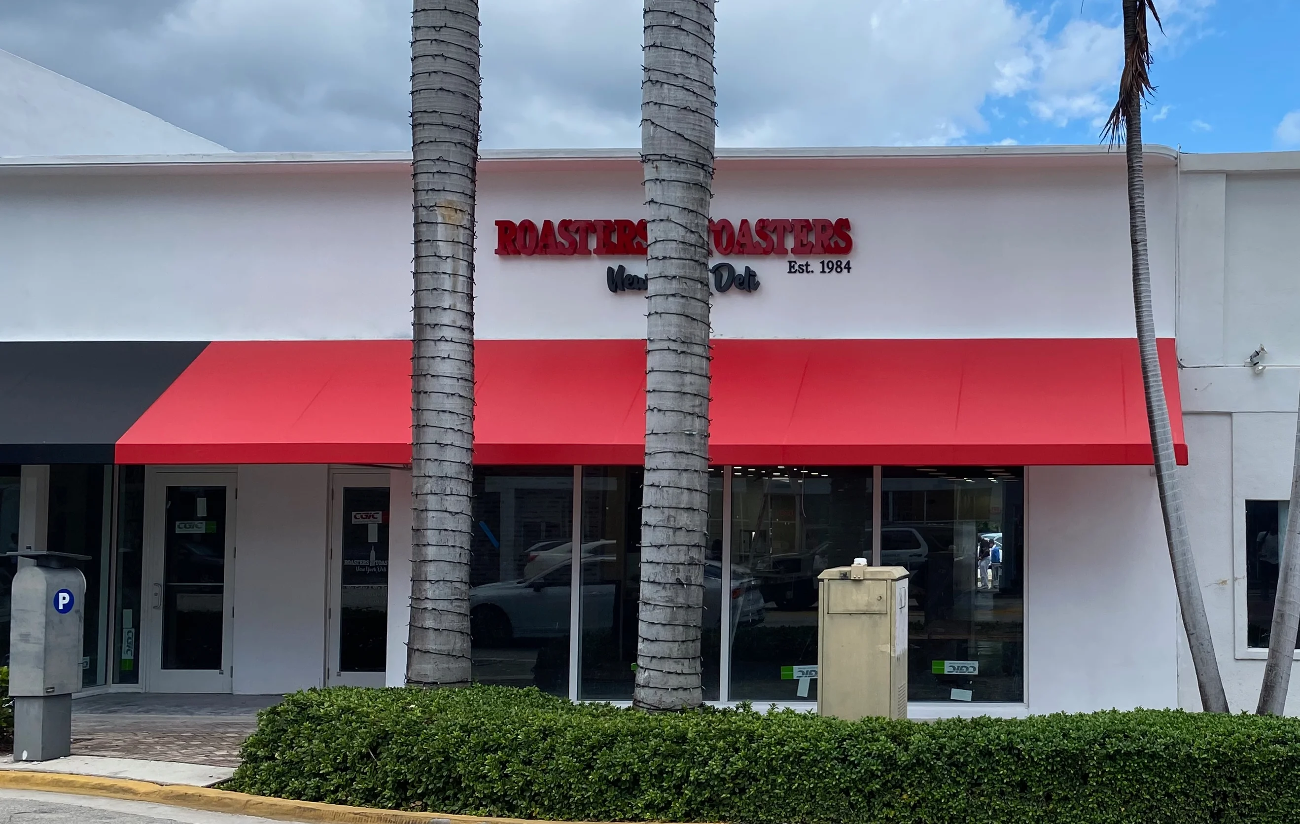 Exterior view of Roasters & Co. restaurant with red awning and palm trees.