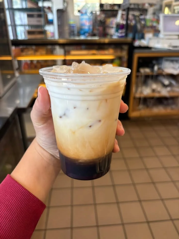 A cold beverage in a clear cup showing layers of iced coffee and cream, with ice cubes visible at the top.