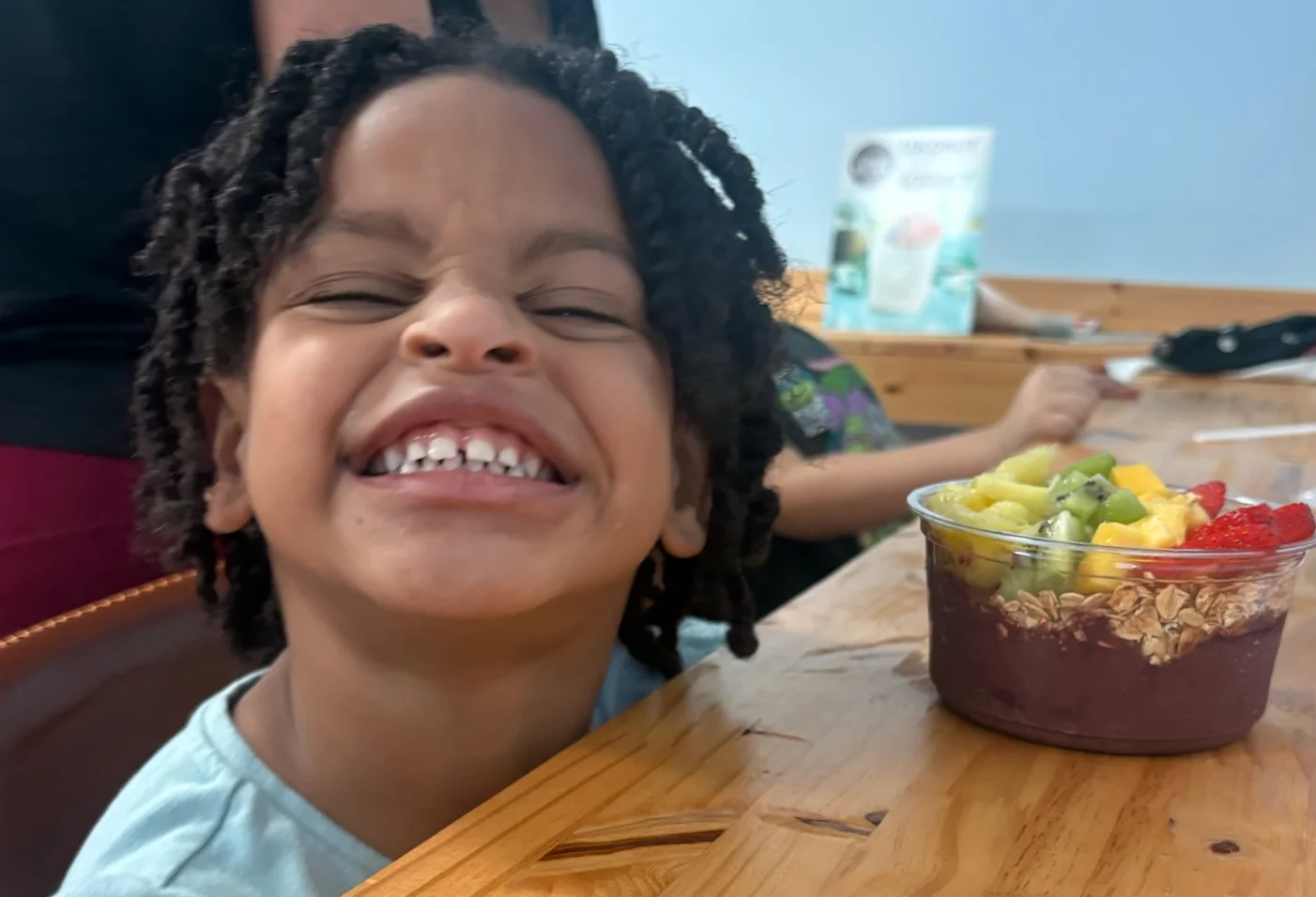 Child smiling with a colorful acai bowl in a cozy cafe
