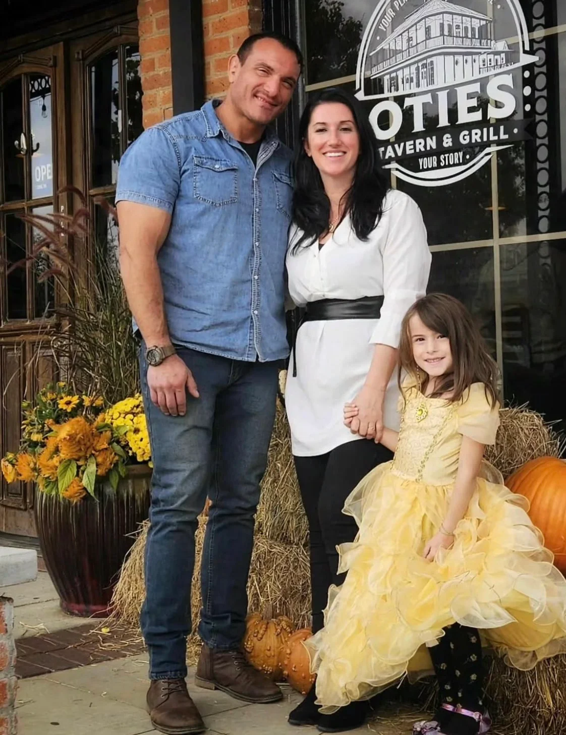 A family poses together outside a restaurant, surrounded by pumpkins and autumn decorations.