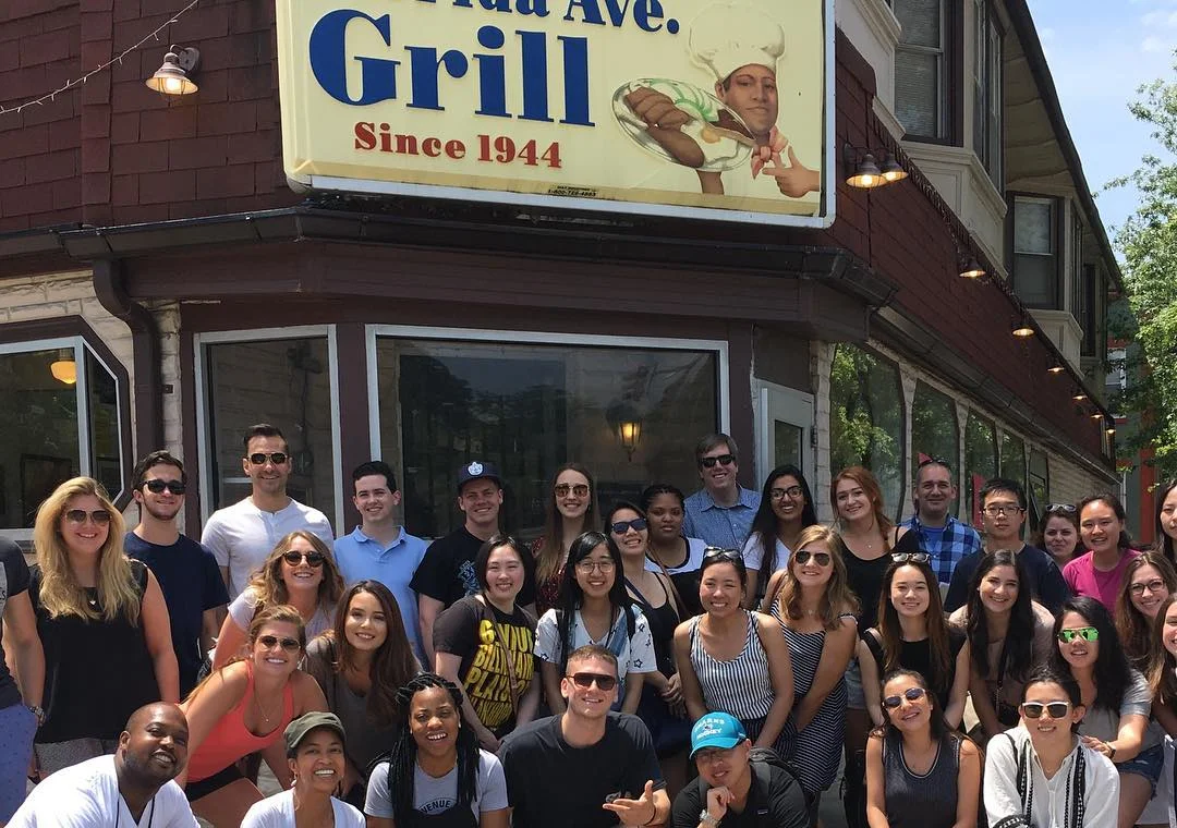 Large restaurant group posing outside Avenue Grill storefront
