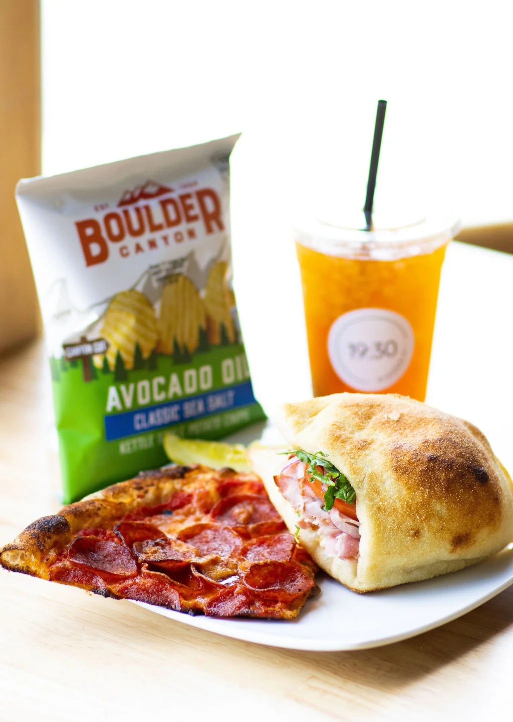 Pepperoni pizza slice with a sandwich and chips on a plate