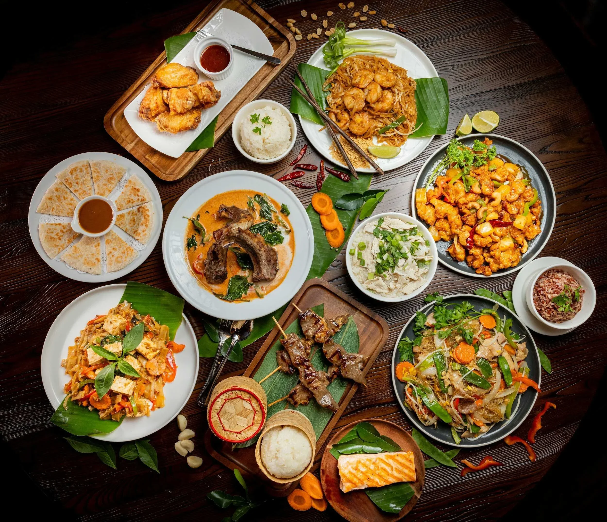 Assorted Asian dishes including pad thai and curry on a wooden table