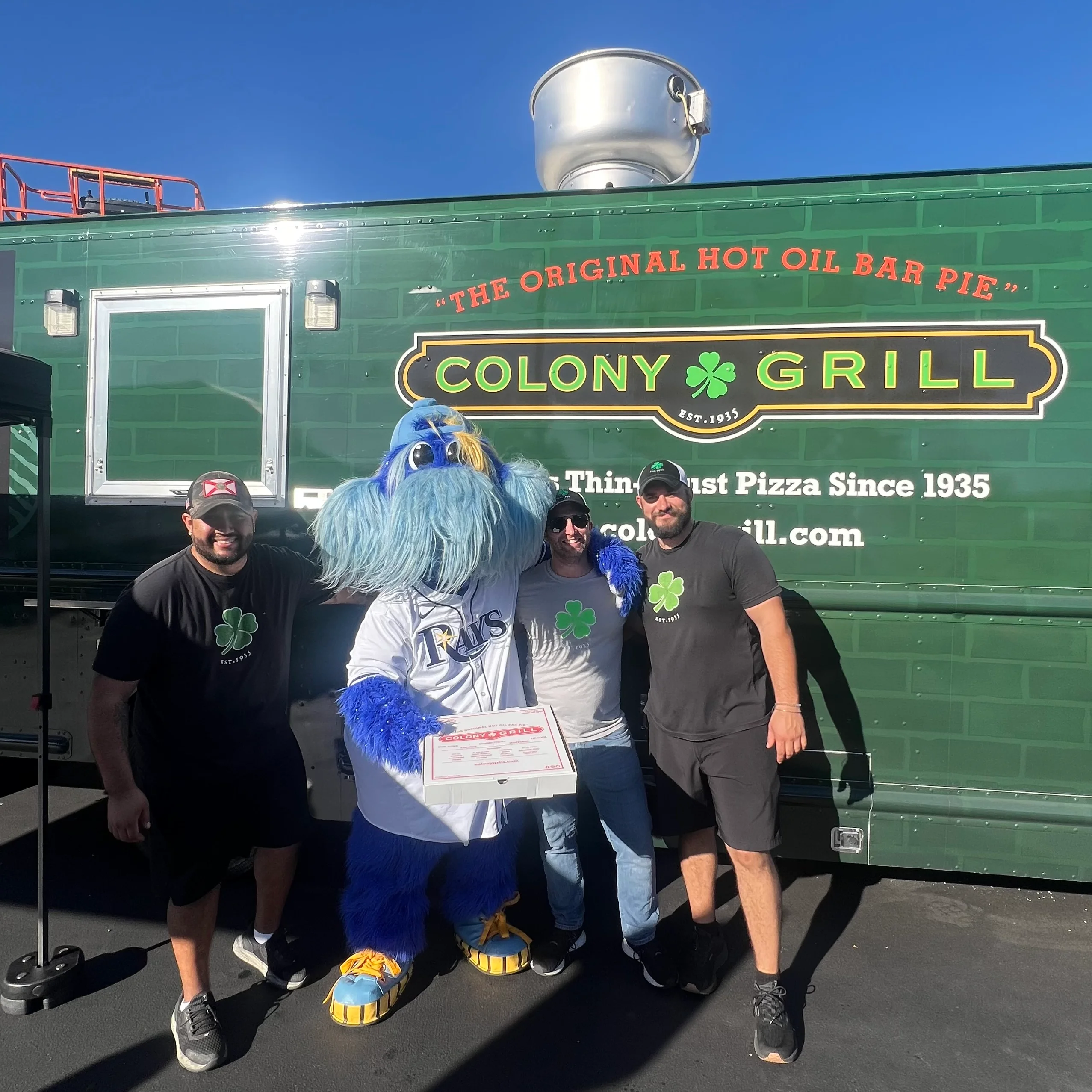 Colony Grill food truck with mascot and staff celebrating pizza